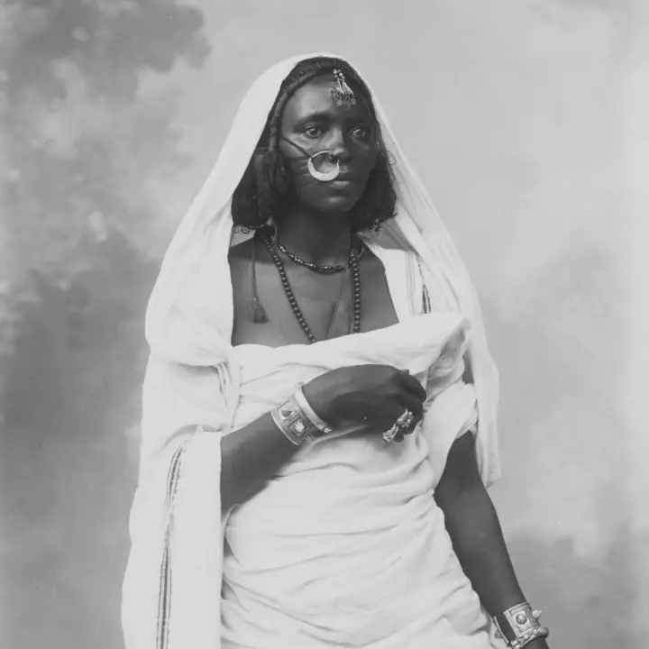 Retrato de uma mulher africana vestida com traje tradicional, usando jóias decorativas.